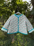 Front view of Teal Paisley Quilted Jacket size 4T — teal paisley cotton with white cross-hatch quilting, bright teal binding, and round white buttons, displayed on a hanger outdoors