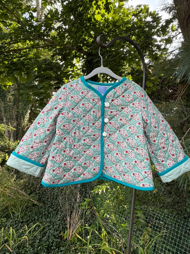 Front view of Teal Paisley Quilted Jacket size 4T — teal paisley cotton with white cross-hatch quilting, bright teal binding, and round white buttons, displayed on a hanger outdoors