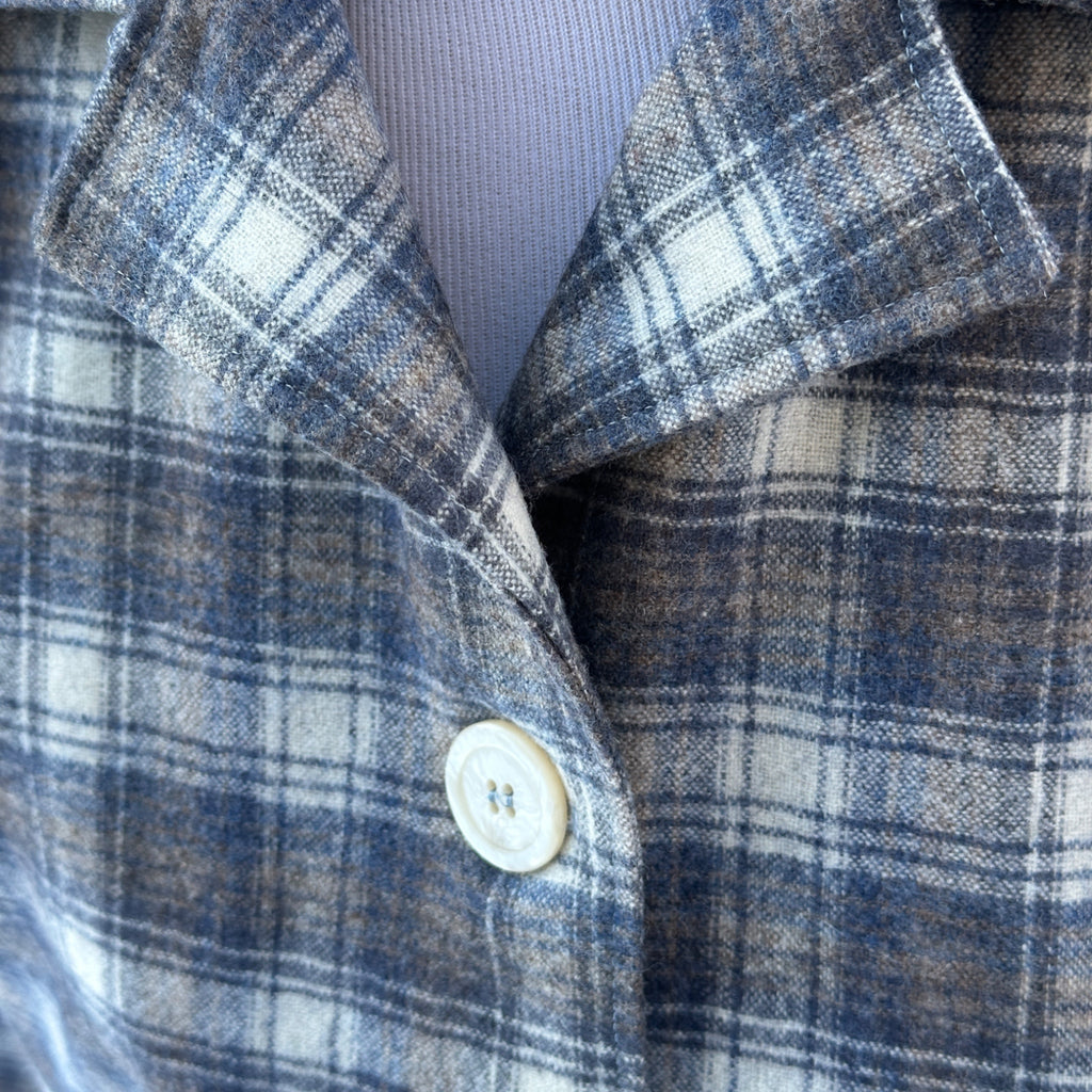Close-up of a plaid shirt collar with a button, featuring blue, gray, and brown colors.