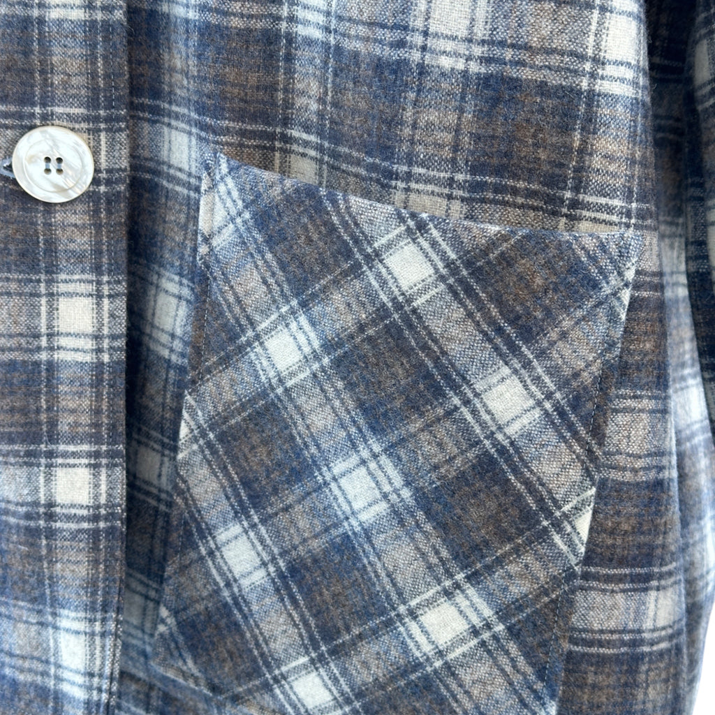 Close-up of a plaid fabric with a button, showing blue, white, and cream colors on bias cut pocket.