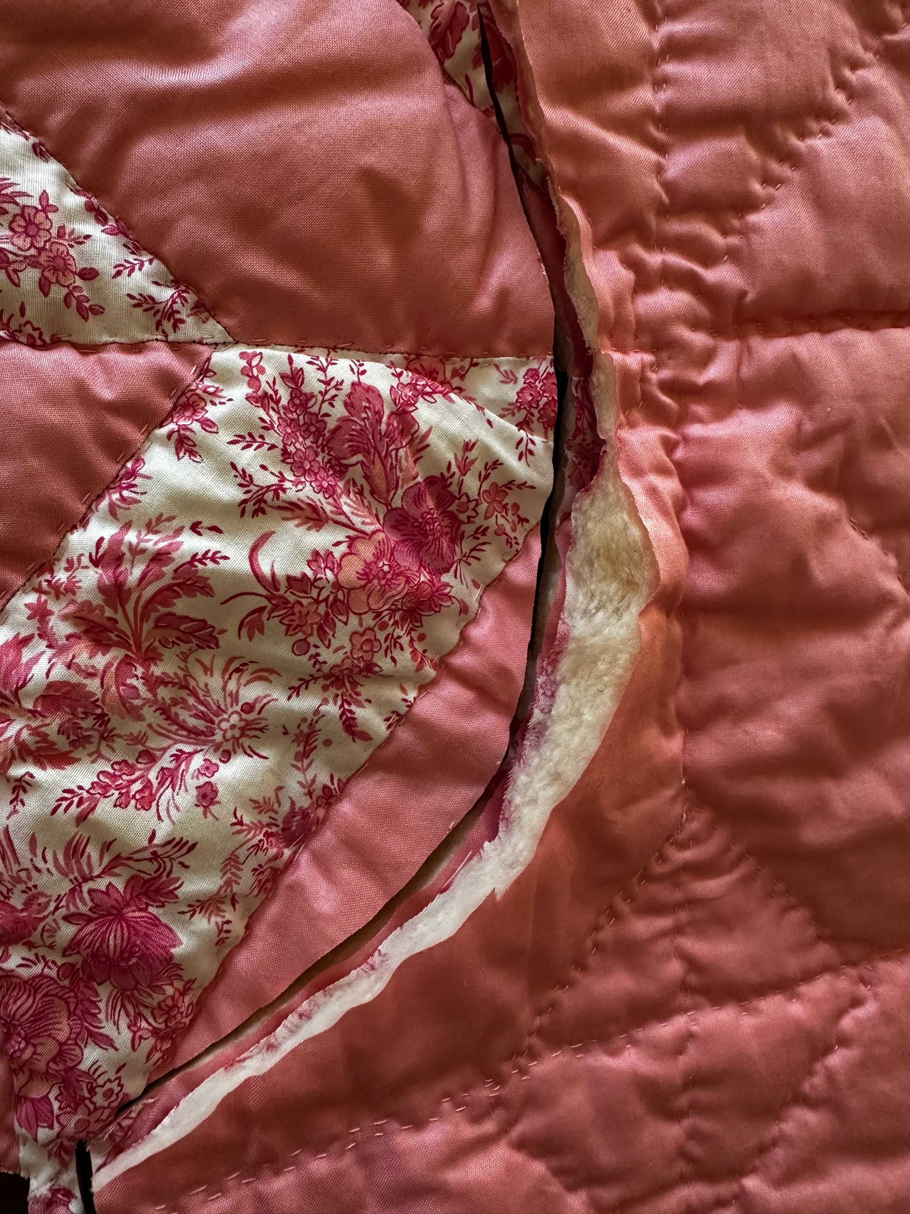 Close-up of The Chatham Quilt fabric — peach solid and white with deep pink floral toile patchwork, original hand quilting with soft cotton batting visible at the seam.