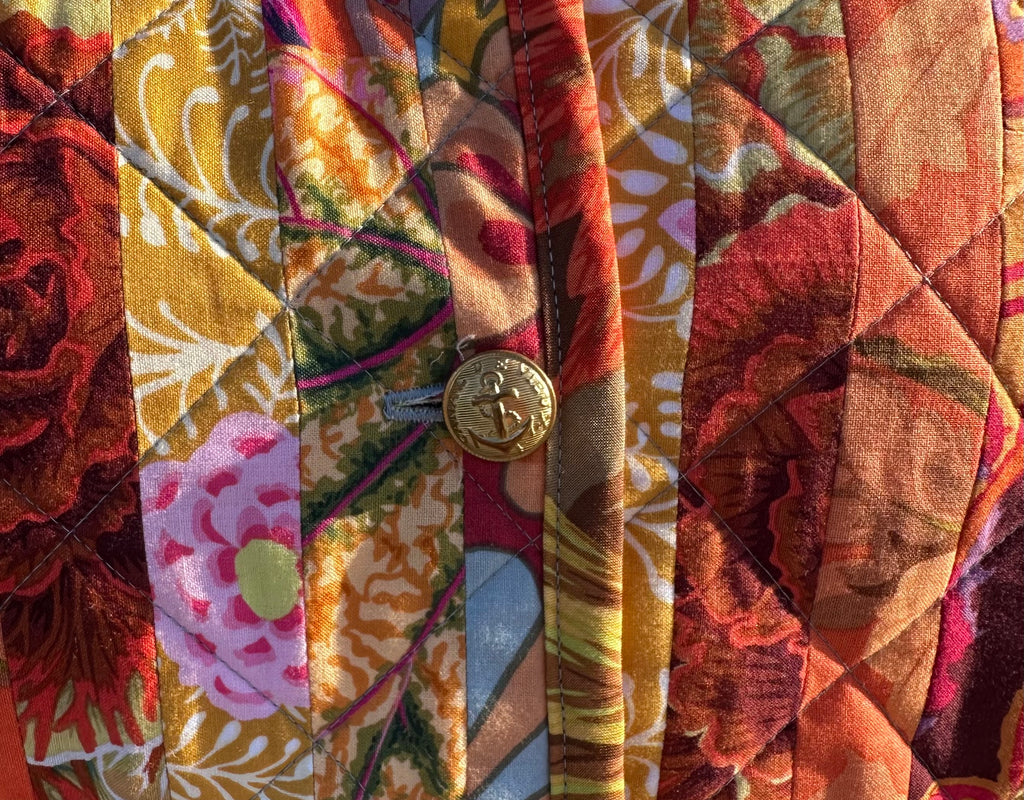 Close-up of a patterned fabric with Cafe Fassett fabric designs in warm colors with gold military buttons. 