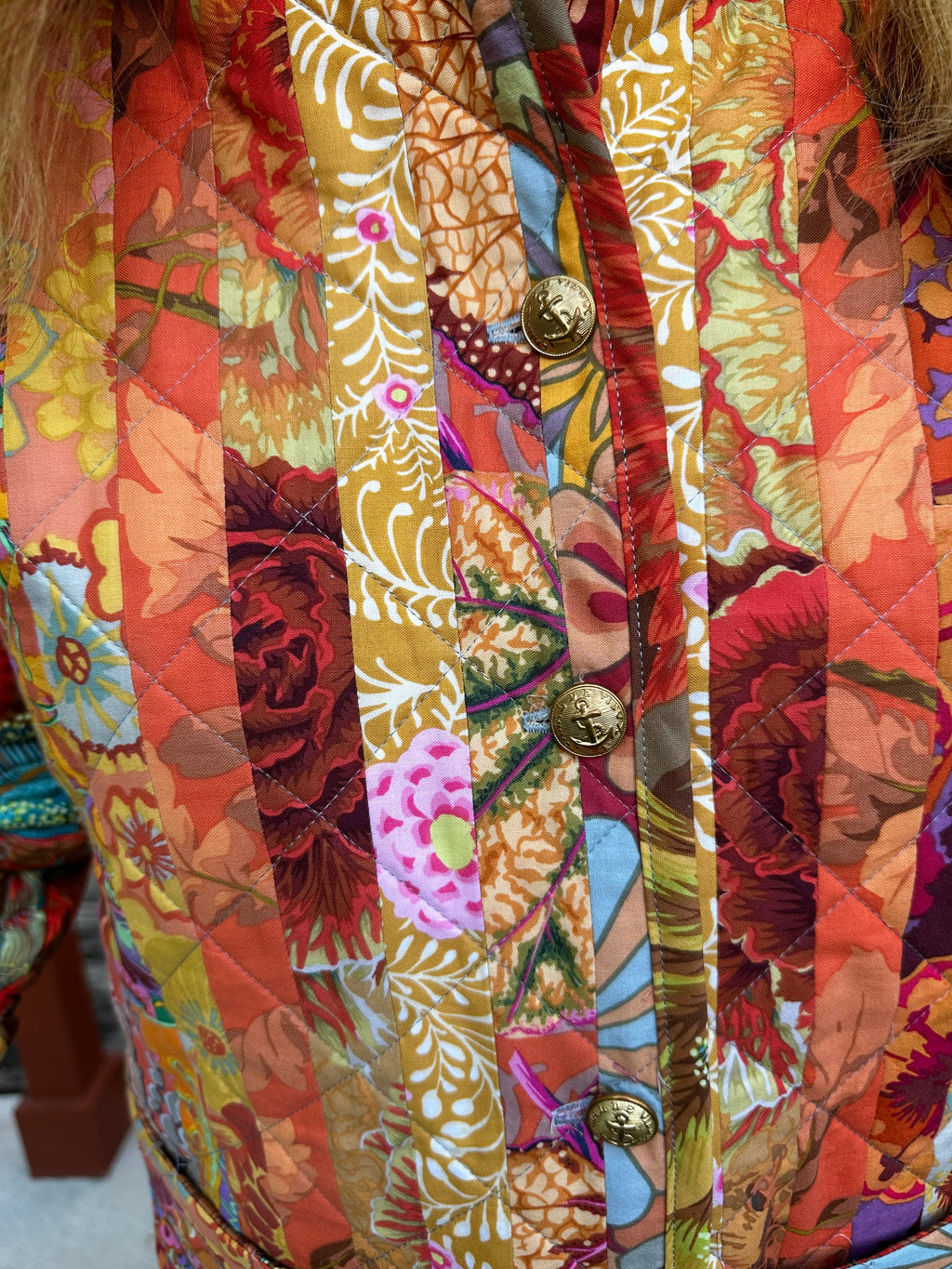 Close-up of a colorful floral-patterned quilted coat with gold military buttons.