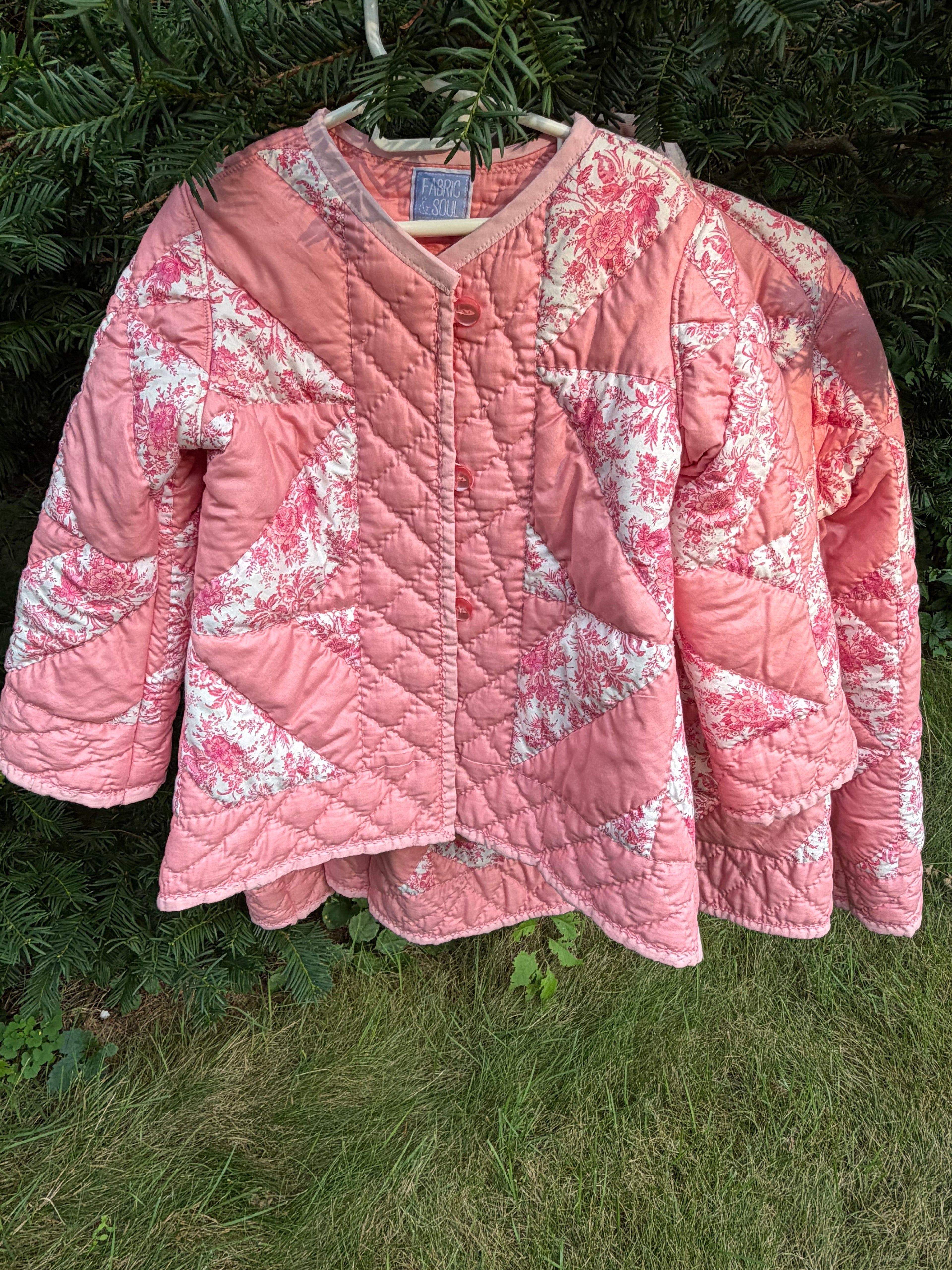 The Chatham Quilt daughter's coat — front view, hanging outdoors. Peach and pink floral toile patchwork pinwheel star pattern, V-neckline, button front, children's size 6/7. Fabric & Soul Signature Collection.