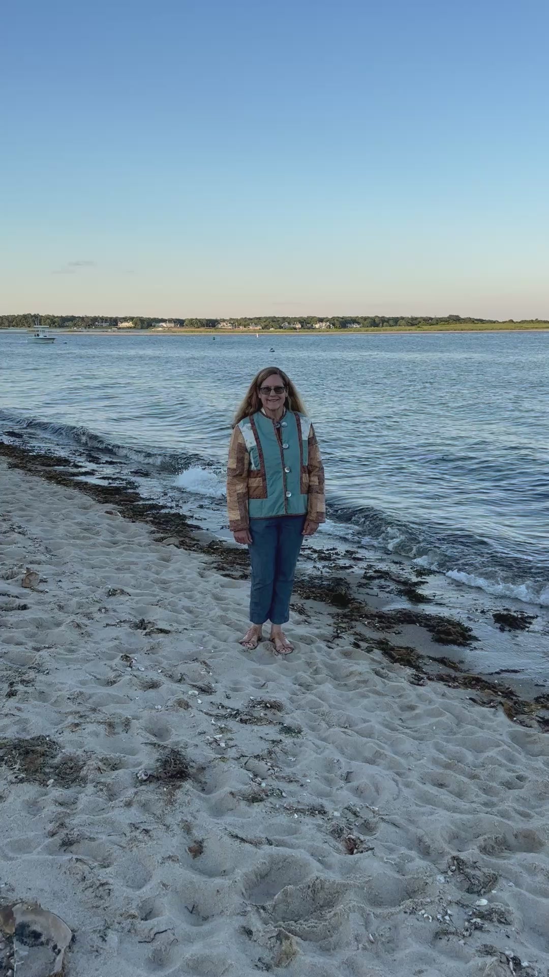 Handmade quilted jacket in motion — repurposed vintage wall hanging with patchwork sleeves in warm tans, browns, and teal, worn on Cape Cod beach. Women's Large, one-of-a-kind wearable art by Fabric & Soul, Cotuit MA.