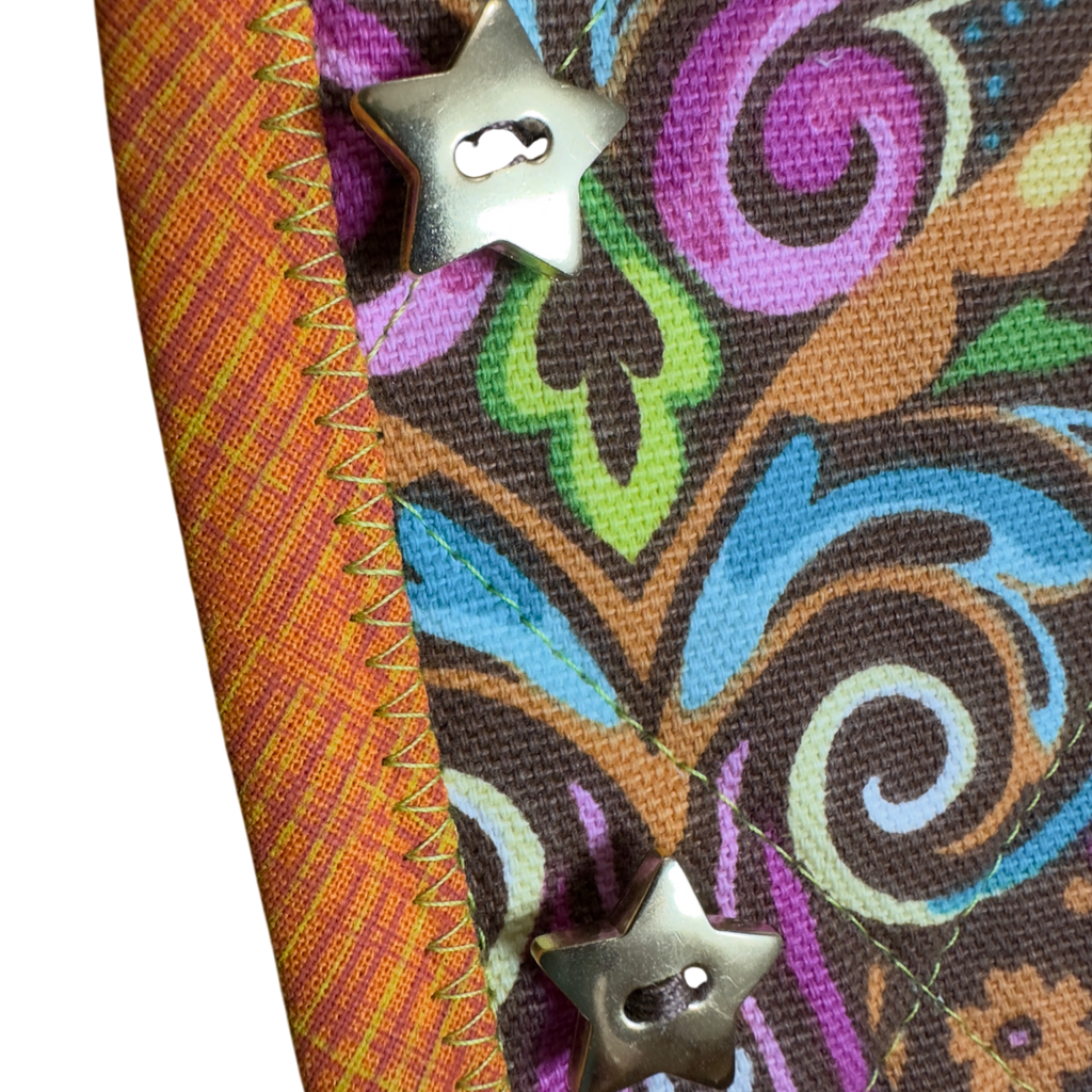 Colorful fabric with intricate patterns and star-shaped buttons and orange and yellow binding